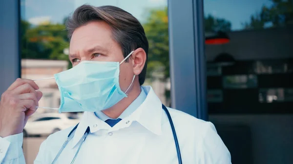 Arzt zieht medizinische Maske ab und schaut in der Nähe der Klinik weg — Stockfoto