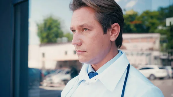 Portrait of serious doctor looking away near blurred clinic — Stock Photo