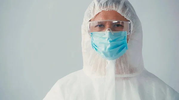 Portrait of immunologist in ppe suit and goggles with medical mask looking at camera isolated on grey — Stock Photo