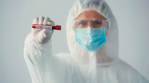 Blurred doctor in hazmat suit showing negative coronavirus test isolated on grey — Stock Photo