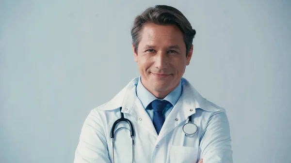 Positive doctor in white coat and with stethoscope smiling at camera isolated on grey — Stock Photo