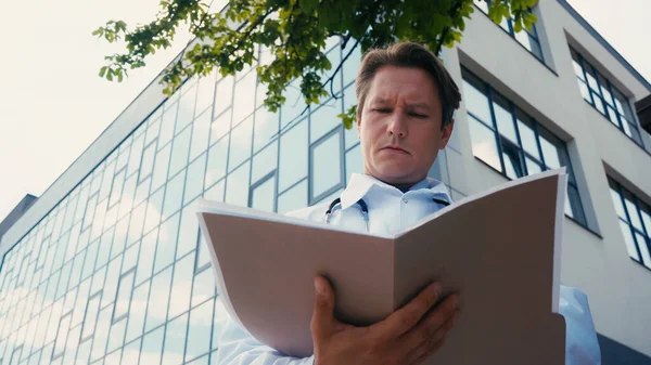 Low angle view of doctor looking in folder with documents near hospital building — Stock Photo