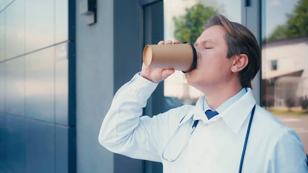 Médico con estetoscopio beber café cerca de la construcción de la clínica - foto de stock