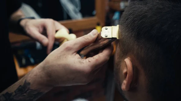 Обрізаний вид татуйованого перукаря обрізання волосся людини з затискачем в салоні — стокове фото