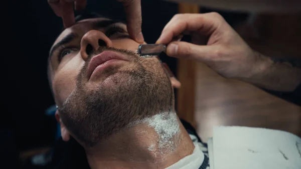 Barber shaving beard of client with razor in salon — Stock Photo