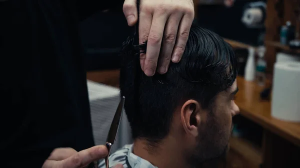 Hairdresser holding scissors and hair of client in hairdressing cape in salon — Stock Photo