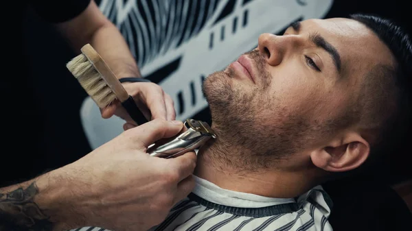 Barber trimming beard of customer in blurred barbershop — Stock Photo