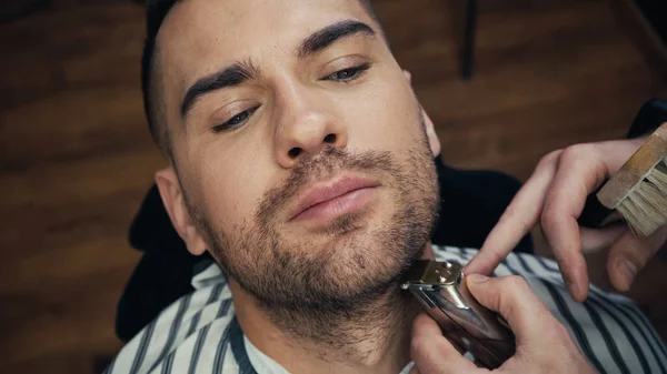 Vue du dessus du barbier tenant la brosse et la barbe de coupe du client dans le salon de coiffure — Photo de stock