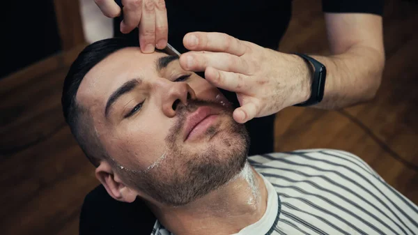 High angle view of barber shaving brunette client in barbershop — Stock Photo