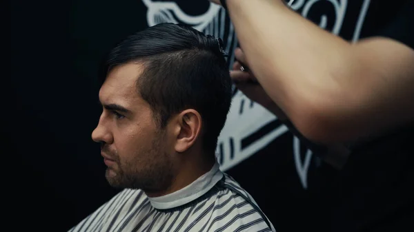 Man in hairdressing cape sitting near hairstylist in barbershop — Stock Photo