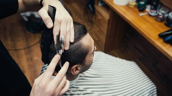 Visão aérea do barbeiro cortando o cabelo do homem na capa de cabeleireiro borrada na barbearia — Fotografia de Stock