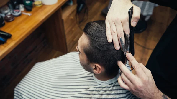 Overhead view of hairstylist cutting hair of man in blurred salon — Stock Photo