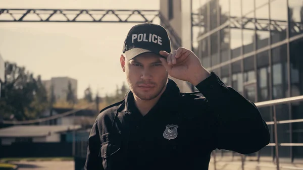 Junger Polizist blickt in Kamera und passt Mütze im Freien an — Stockfoto