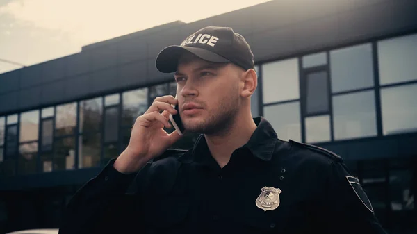 Policeman in uniform and badge talking on smartphone on urban street — Stock Photo