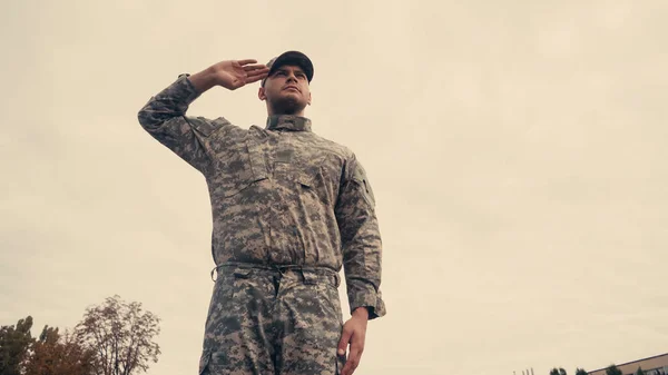 Low angle view of soldier saluting with cloudy sky at background outdoors — Stock Photo