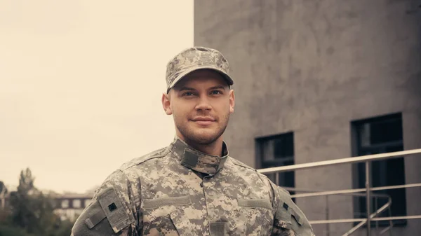 Soldat souriant en uniforme et casquette regardant loin tout en marchant à l'extérieur — Photo de stock