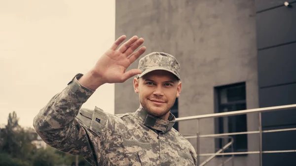 Soldado sonriente en uniforme y saludo de gorra mientras camina al aire libre - foto de stock