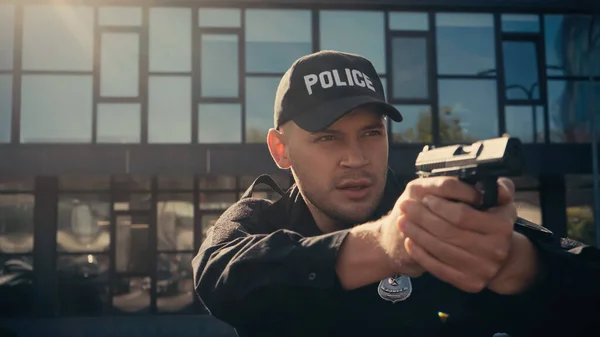 Focused policeman in uniform and cap holding gun on urban street — Stock Photo