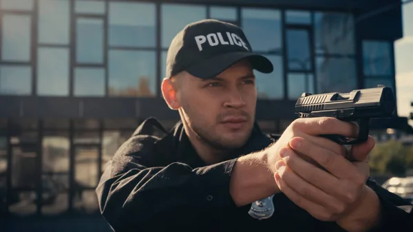 Policía en uniforme y gorra sosteniendo arma en calle urbana - foto de stock