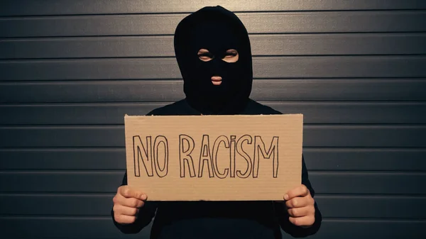 Man in balaclava holding placard with no racism lettering near building — Stock Photo