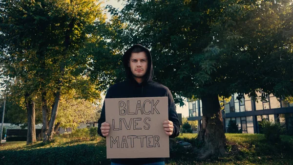 Молодой человек в капюшоне держит плакат с черными жизнями материи буквы снаружи — стоковое фото