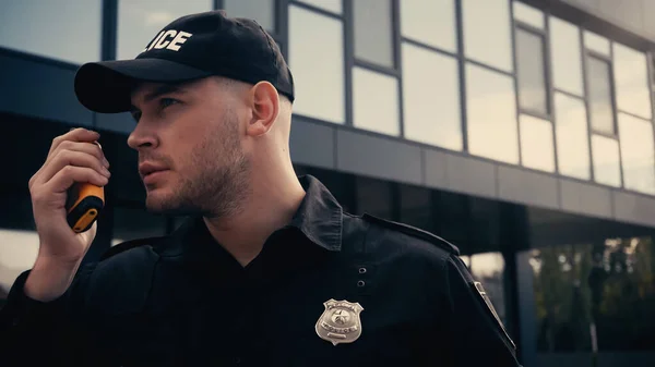 Jeune policier en uniforme et casquette utilisant talkie walkie à l'extérieur — Photo de stock