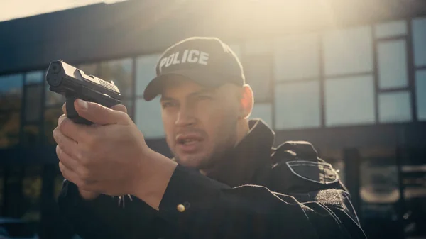 Jovem policial de uniforme e boné com letras apontando com arma na rua urbana — Fotografia de Stock