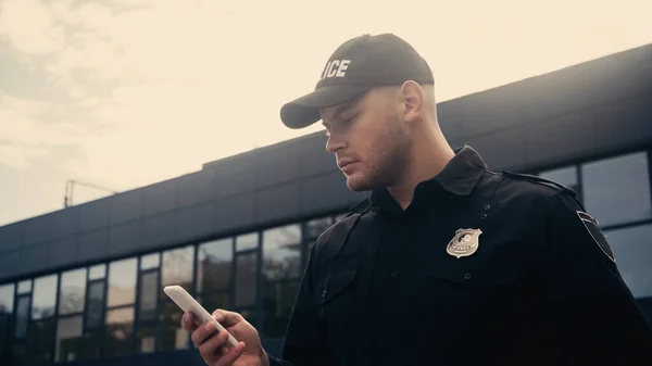 Jovem policial de uniforme com crachá usando smartphone na rua urbana — Fotografia de Stock