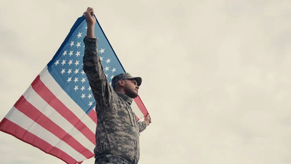 Low angle view of soldier in uniform and cap holding american flag outdoors — Stock Photo