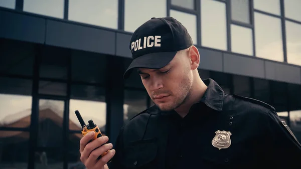 Policial concentrado em uniforme e boné segurando walkie talkie ao ar livre — Fotografia de Stock