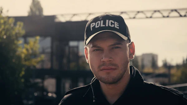 Jovem policial em boné com letras policiais e uniforme olhando para a câmera — Fotografia de Stock