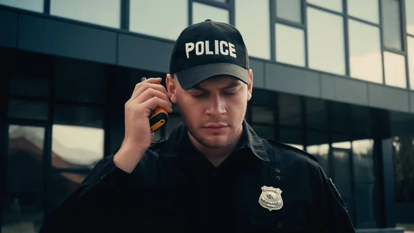Policier en uniforme et casquette écoute des informations tout en tenant talkie walkie dans la rue — Photo de stock