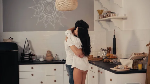 Jovem morena de camisa branca abraçando namorado na cozinha moderna — Fotografia de Stock