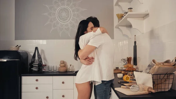 Brunette young woman in white shirt hugging boyfriend in modern kitchen — Stock Photo