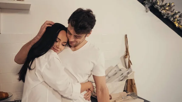 Brunette young woman in white shirt hugging boyfriend stroking her hair in kitchen — Stock Photo