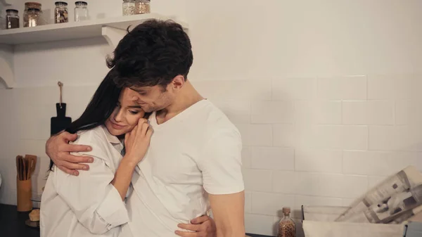 Brunette young woman in white shirt hugging pleased boyfriend in t-shirt — Stock Photo