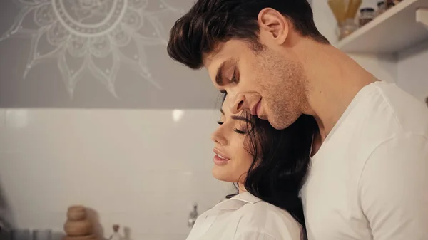 Feliz joven en camisa blanca y novio en camiseta sonriendo en la cocina - foto de stock