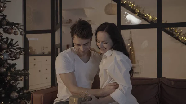 Feliz pareja mirando envuelto caja de regalo cerca de árbol de Navidad decorado - foto de stock