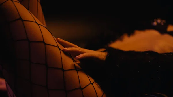 Ausgeschnittene Ansicht einer sexy Frau, die Netzstrumpfhosen auf schwarzem Hintergrund berührt — Stockfoto