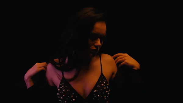 Sexy morena mujer en sujetador quitándose la blusa aislado en negro - foto de stock