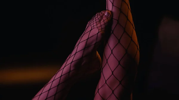 Cropped view of legs of woman in fishnet tights on black background — Stock Photo