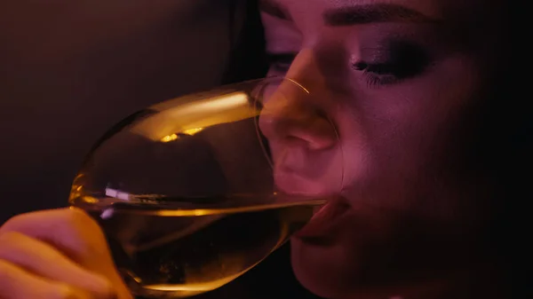 Jeune femme buvant du vin sur fond noir avec éclairage — Photo de stock