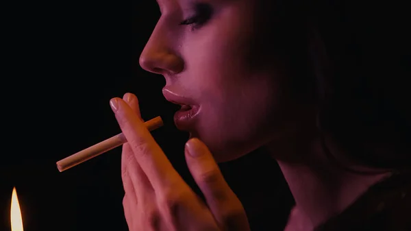 Vue latérale de la femme tenant la cigarette près du feu isolé sur noir — Photo de stock