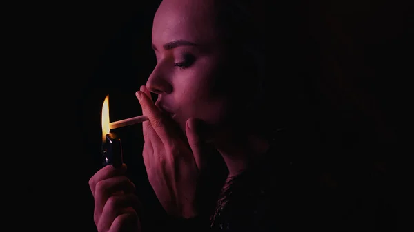 Giovane donna con accendino e sigaretta isolati su nero con illuminazione — Foto stock