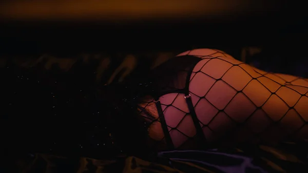 Обрезанный вид ягодиц сексуальной женщины в сетчатых колготках на черном фоне — стоковое фото