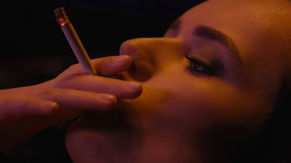 Close up view of young woman smoking cigarette isolated on black — Stock Photo