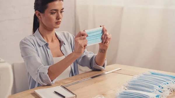 Brünette Näherin hält medizinische Maske neben Lineal und Notizbuch in der Werkstatt — Stockfoto