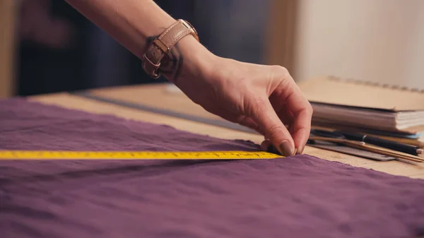 Cropped view of seamstress measuring cloth near notebook on table in atelier — Stock Photo