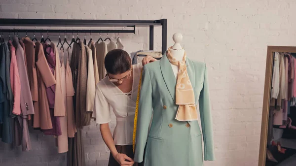 Designer mesurant veste élégante sur mannequin en atelier — Photo de stock