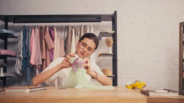 Designer em óculos fazendo vestido em pequeno manequim no atelier — Fotografia de Stock